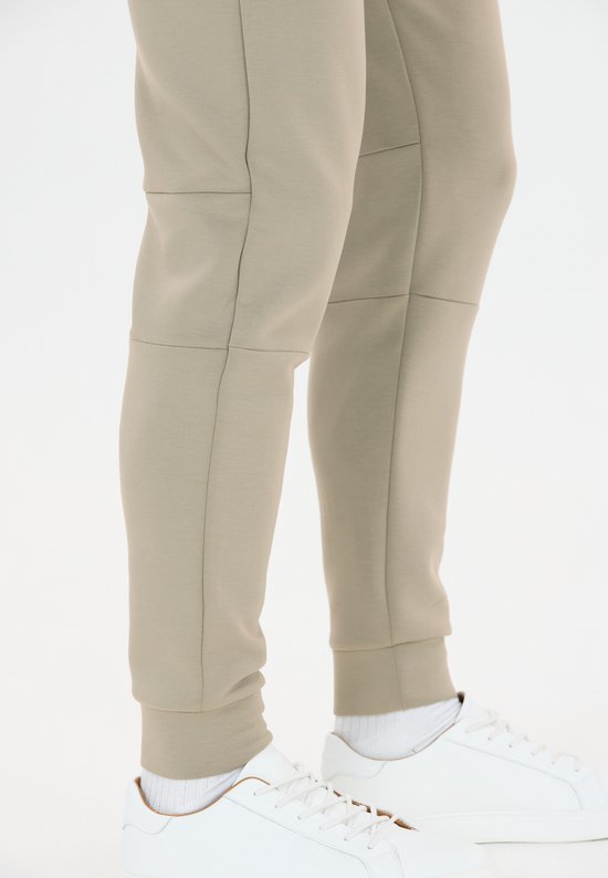 Onderkant van beige trainingsbroek met paneeldetails op de benen, met witte sneakers.