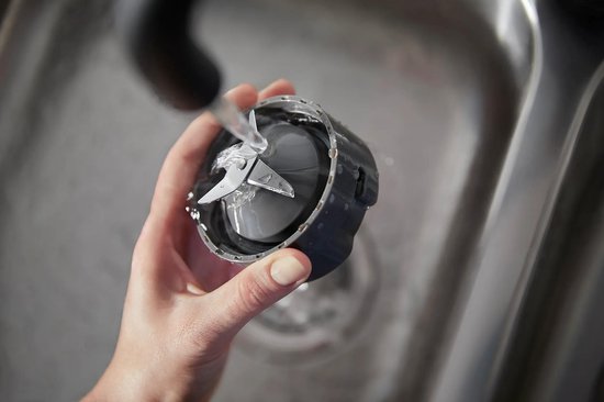 Hand wast een blenderopzetstuk met messen onder een kraan.