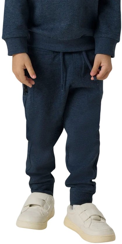 Onderlichaam van een jongen in een donkerblauwe joggingbroek en witte sneakers.