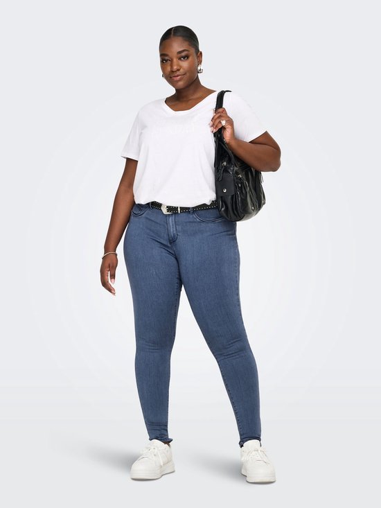 Model draagt een blauwe skinny jeans met een witte t-shirt, zwarte riem en tas.