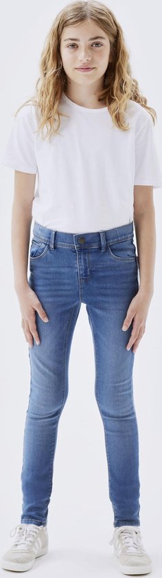 Meisje met lang blond haar in een witte T-shirt en een blauwe skinny spijkerbroek.