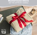 Een zandkleurige Blumtal deken, verpakt met een rood lint, als cadeau.