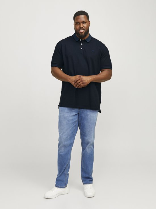 Donkerblauw poloshirt met korte mouwen, gedragen door een man met lichte spijkerbroek en witte sneakers.