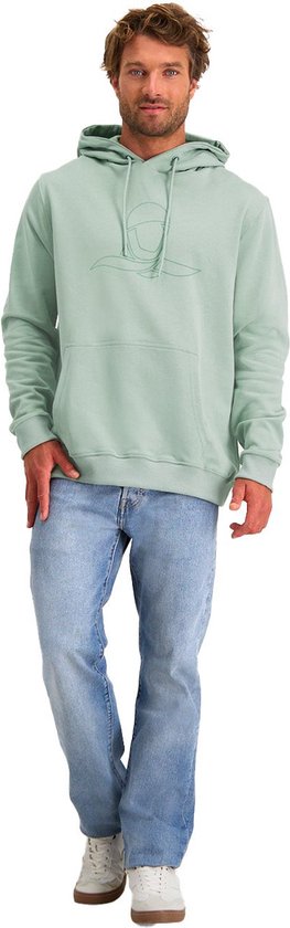 Staande man in mintgroene hoodie met logo en jeans op witte achtergrond.
