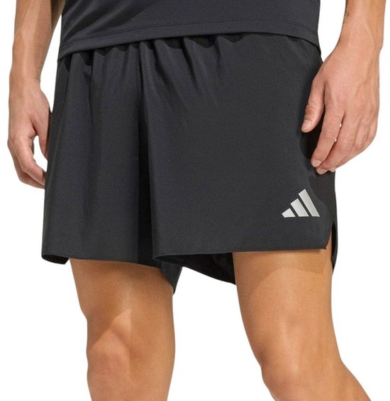 Model draagt een zwarte korte broek met zilverkleurige Adidas-logo's en split aan de zijkant.