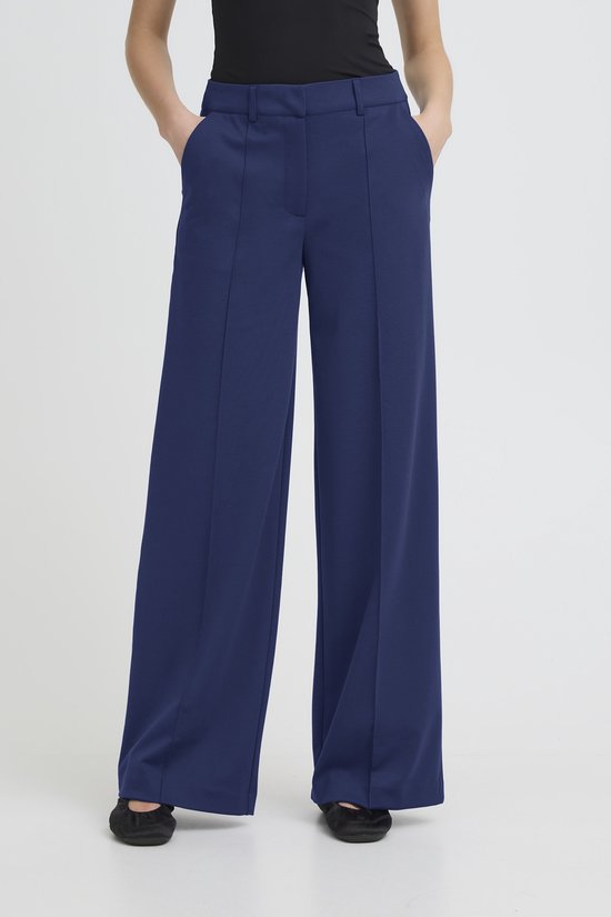 Model van voren gezien in een donkerblauwe, wijde broek met rechte pijpen en een hoge taille.