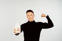 Een gespierde man in een zwart coltrui poseert met een fles 'MEGA SPORT'.