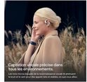 Vrouw met blonde paardenstaart draagt witte Shokz oordopjes, luisterend naar muziek in een veld.