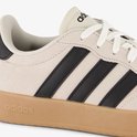 Close-up van beige Adidas sneaker met zwarte strepen en gummen zool met logo.