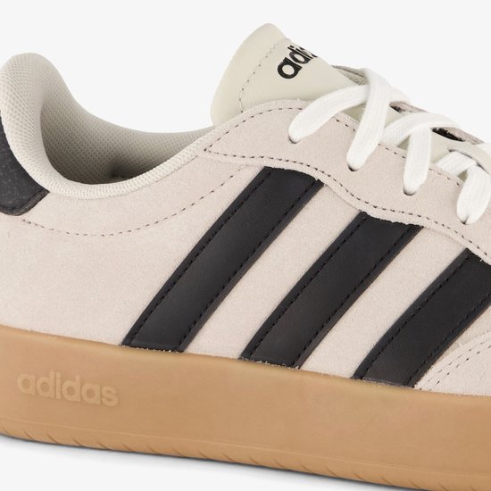 Close-up van beige Adidas sneaker met zwarte strepen en gummen zool met logo.