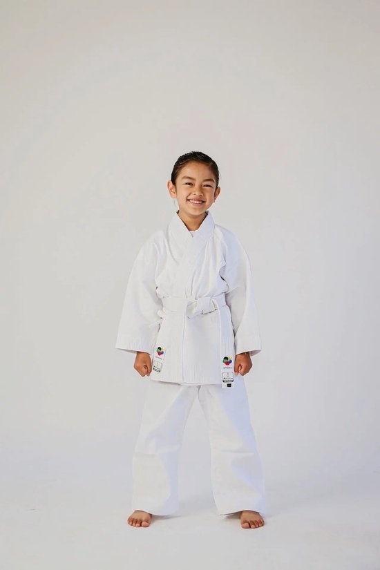 Fille souriante en uniforme de karaté blanche avec ceinture blanche, debout, fond blanc.