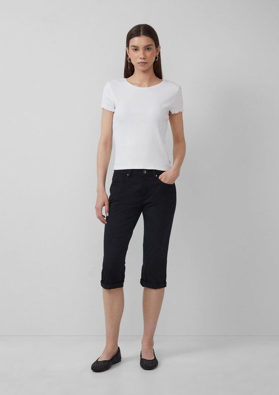Model in witte top en zwarte capri-jeans met hand in zak, frontaal weergegeven.
