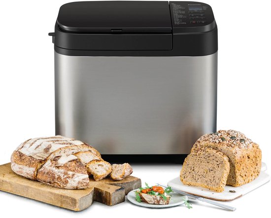 Zilverkleurige broodbakmachine met gesneden brood en een heel brood met zaden erop.