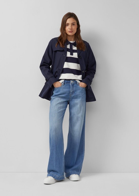 Model in donkerblauwe trenchcoat met ceintuur, gestreept shirt en wijde jeans.