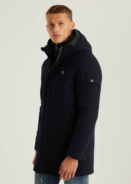 Man met donkerblauwe wollen parka met capuchon, gelaagd met een zwarte pufferjas.