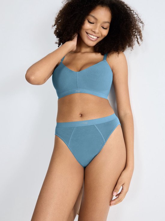Model draagt blauwe Sloggi BH met V-hals en bijpassende slip. BH heeft verstelbare bandjes en een elastische band.