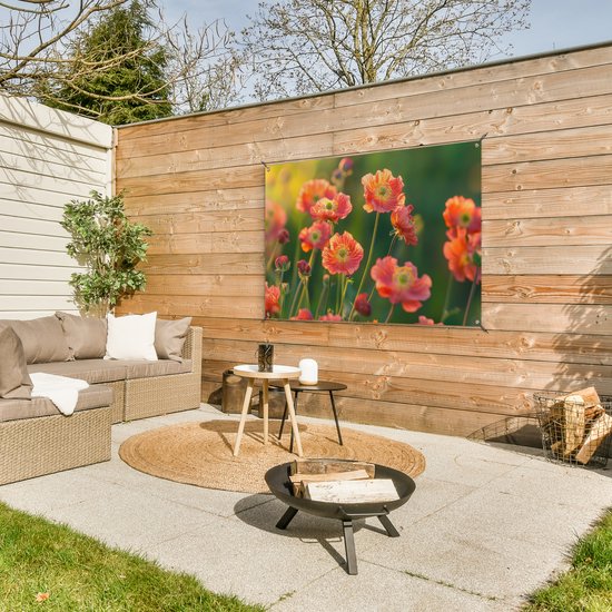 Een tuinposter met oranje klaprozen hangt aan een houten schutting boven een loungeset.