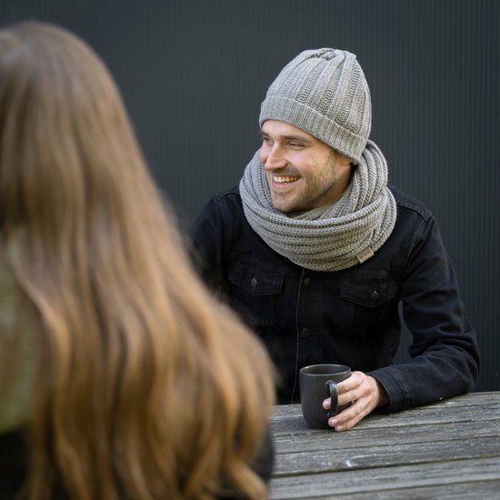 Man met grijze gebreide muts en sjaal, lachend met een mok.
