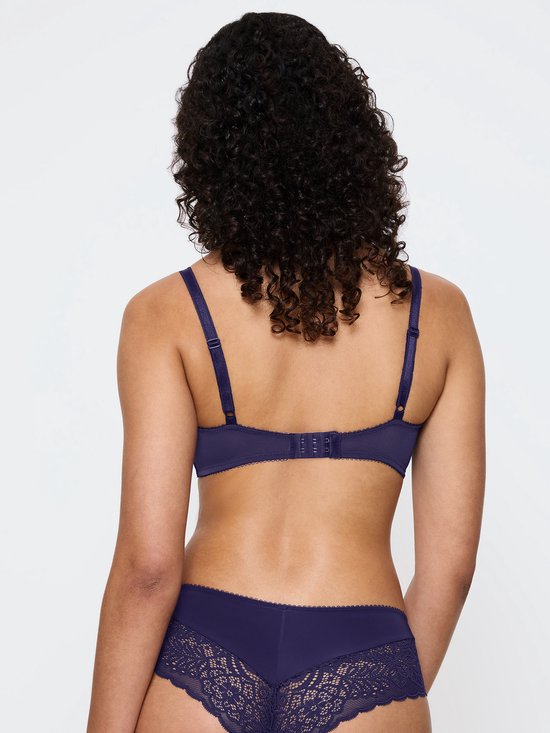 Model met de rug naar voren, draagt een donkerblauwe beha met kanten details en bijpassende slip.