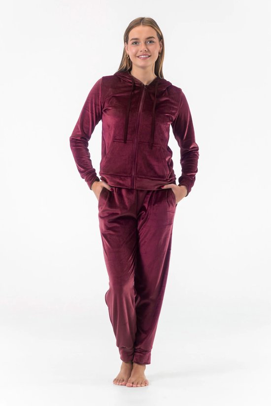 Model draagt een bordeauxrode velours loungewear set. De set bestaat uit een hoodie met rits en zakken, en een joggingbroek.