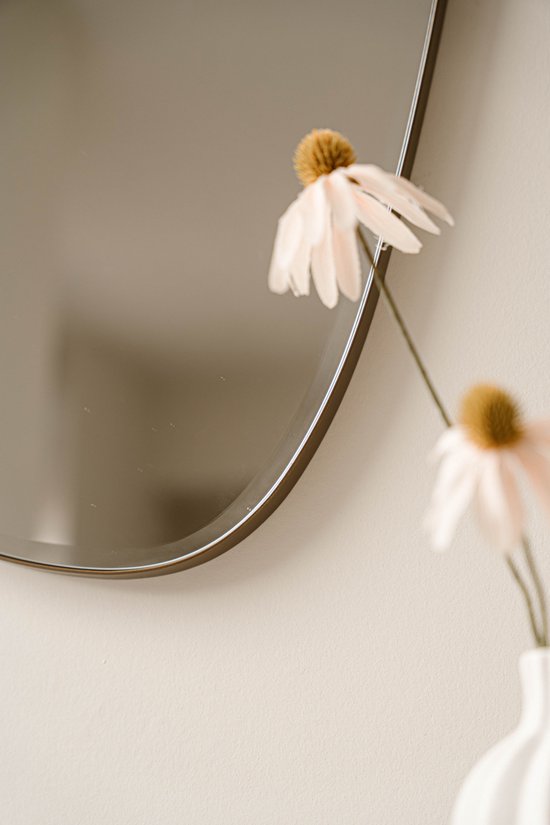 Een donker metalen spiegelrand met subtiele details, naast een bloem.