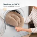 Een beige pluche hondenmand wordt in een wasmachine gestopt.