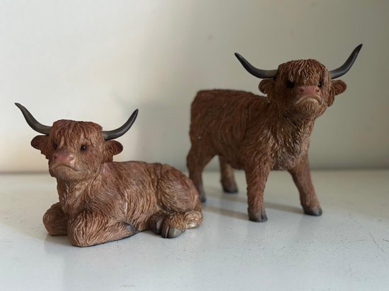 Deux statuettes de vaches Highland brunes, l'une couchée et l'autre debout, avec de longues cornes.