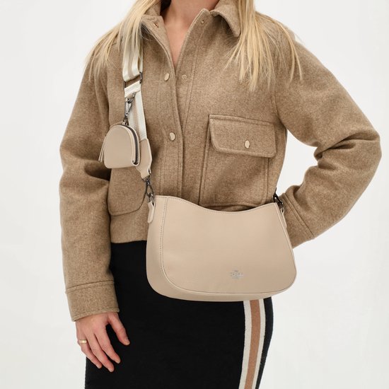 Model met taupekleurige schoudertas van Charm London en bijpassend etui, gedragen met bruine jas en gestreepte rok.