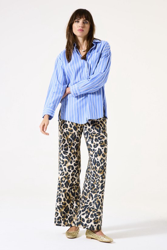 Model in losvallende blauw-wit gestreepte blouse en bruin-zwarte luipaardprint broek met wijde pijpen.