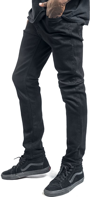 Voeten van een man in zwarte skinny jeans en zwarte hoge Vans sneakers.
