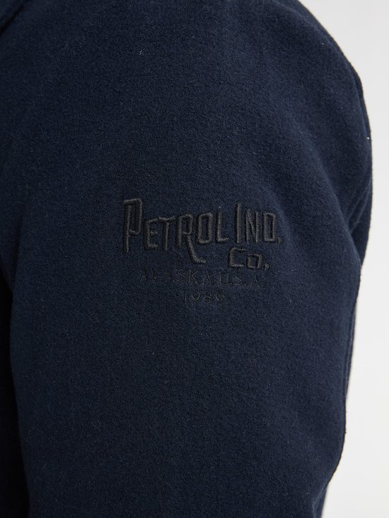 Detail van de tekst 'Petrol Ind. Co. Alaska U.S.A. 1980' op de mouw van een donkerblauwe jas.