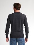 Man staat met zijn rug naar de camera in een donkergrijze gebreide trui en blauwe jeans.