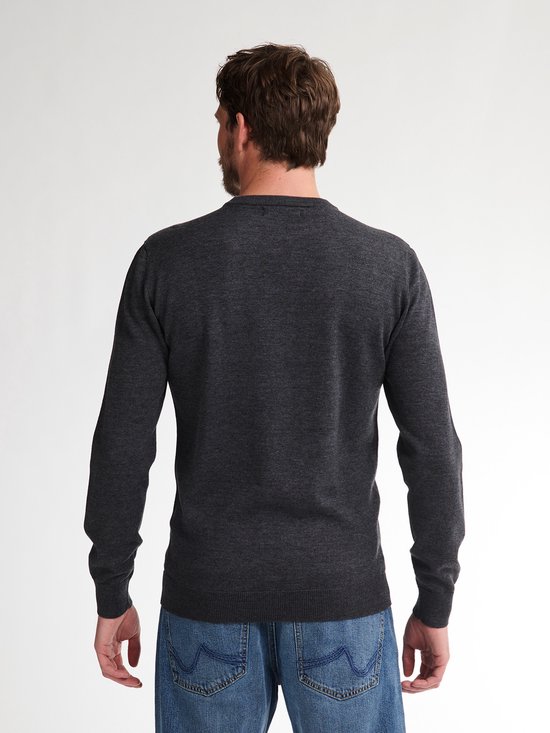 Man staat met zijn rug naar de camera in een donkergrijze gebreide trui en blauwe jeans.