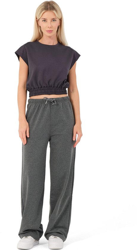 Model met blonde haren draagt een antracietkleurige, wijde joggingbroek met koordje en een kort, donkergrijs topje met pofmouwen.