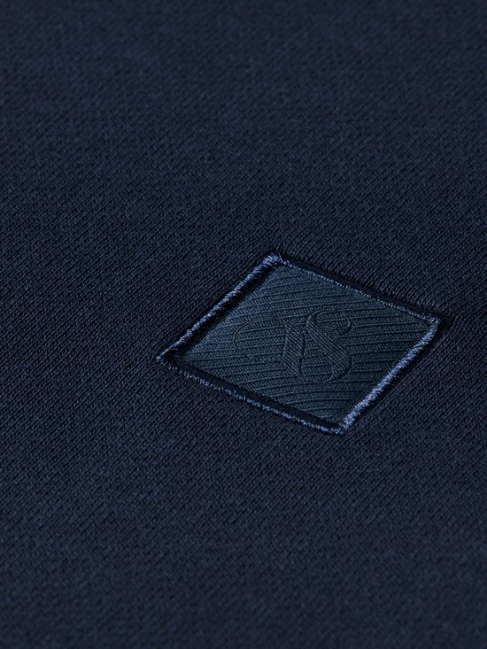 Close-up van het geborduurde vierkante donkerblauwe logo op een donkerblauwe sweater.