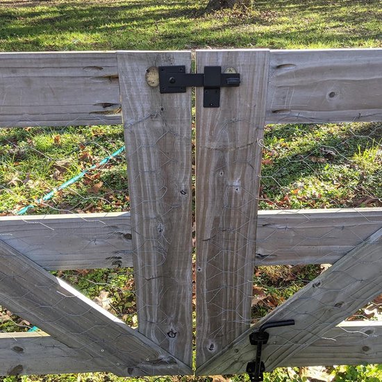Zwarte poortsluiting op een houten dubbele poort, met gaas op de achtergrond.