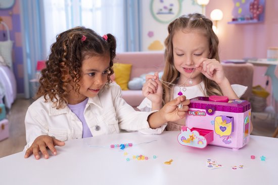 Twee meisjes maken sieraden bij een roze glitter sieradendoos. Eén meisje met krullend haar, de ander met lang blond haar.