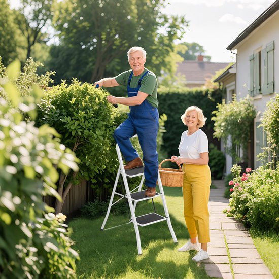 Een man in een overall staat op een witte opvouwbare trap en snoeit een struik in een tuin. Een vrouw met een mand staat ernaast.