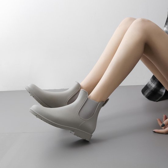 Grijze Chelsea regenlaarzen, met elastische zijkanten, gedragen door een model zittend op de grond.