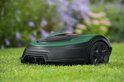 Groene en zwarte robotmaaier op een gazon met bloemen op de achtergrond.