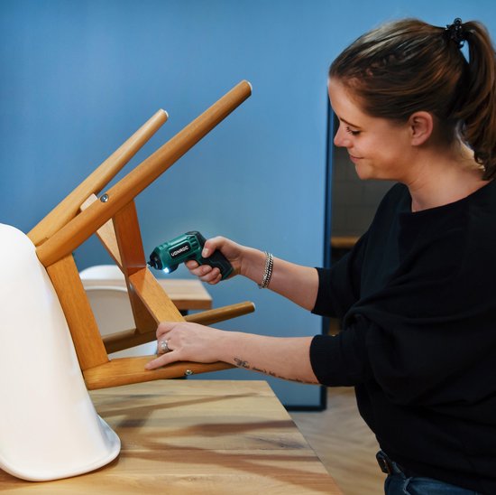Vrouw met bruin haar in paardenstaart monteert een houten stoel met een groene Vonroc accuschroefmachine.