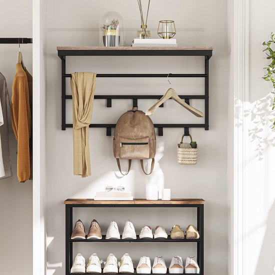 Kapstok met grijze houten plank en zwart metalen frame in een hal. Een sjaal, rugzak, mand en kleding hangen aan de haken. Een spiegel en planten staan op de plank.