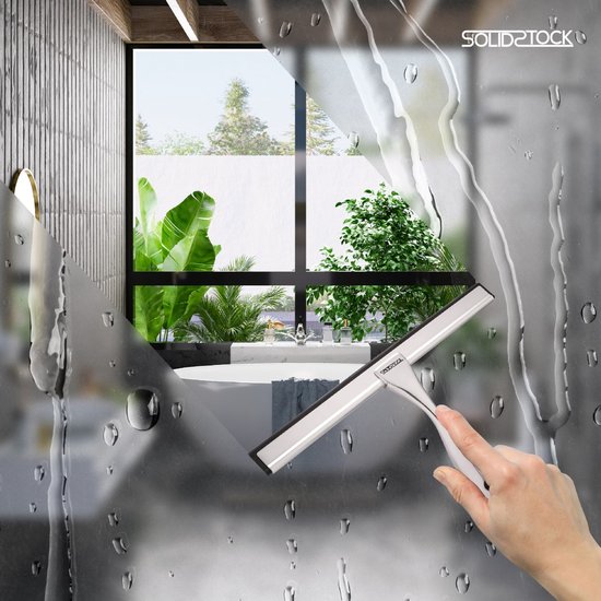 Main avec une raclette de douche en acier inoxydable nettoyant une fenêtre de salle de bain mouillée.
