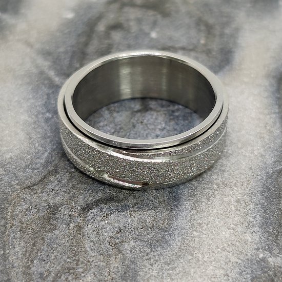 Zilverkleurige ring met een glinsterende, gestreepte band, op een marmeren achtergrond.