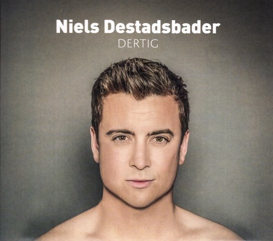Portret van Niels Destadsbader, blote schouders, donker haar, grijze achtergrond.