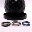 Drie fidgetringen in zilver, zilver/zwart en zilver/blauw naast een zwarte schaal.