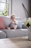 Baby met witte polo en bruine shorts, zittend op een grijze bank, met Sophie de giraf bijtring.