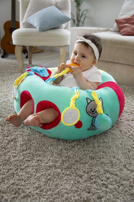 Baby met witte hoofdband kauwt op gele rammelaar in een mintgroen speelzitje.