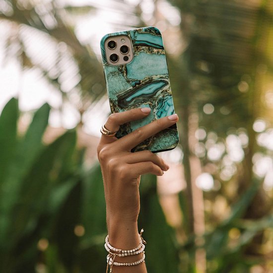 Vrouw houdt een telefoonhoes met groen en goud marmerpatroon omhoog tegen een achtergrond van planten.
