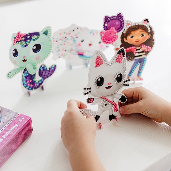 Wit kattenfiguur met strass-steentjes, zittend tussen andere figuren in een knutselset.